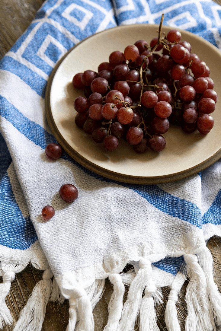 Blue and white hand towels made in pure Turkish cotton with white tassels and a plate of red grapes 