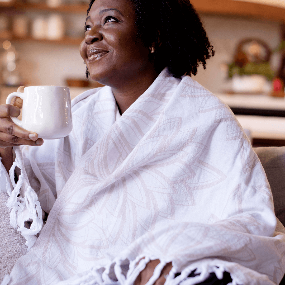 A woman of colour in a green shirt looking off to the side draped in a white Turkish towel.