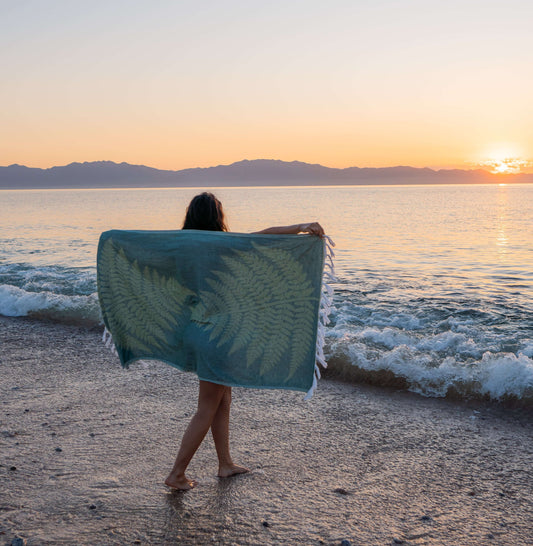 Woman on the beach holing up a green fern Turkish towel