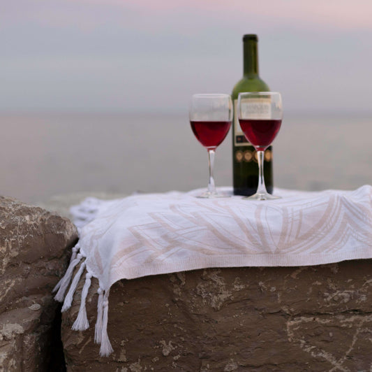 Two glasses of red wine with a bottle of wine sit upon a Turkish towel overlooking the lake on Ontario