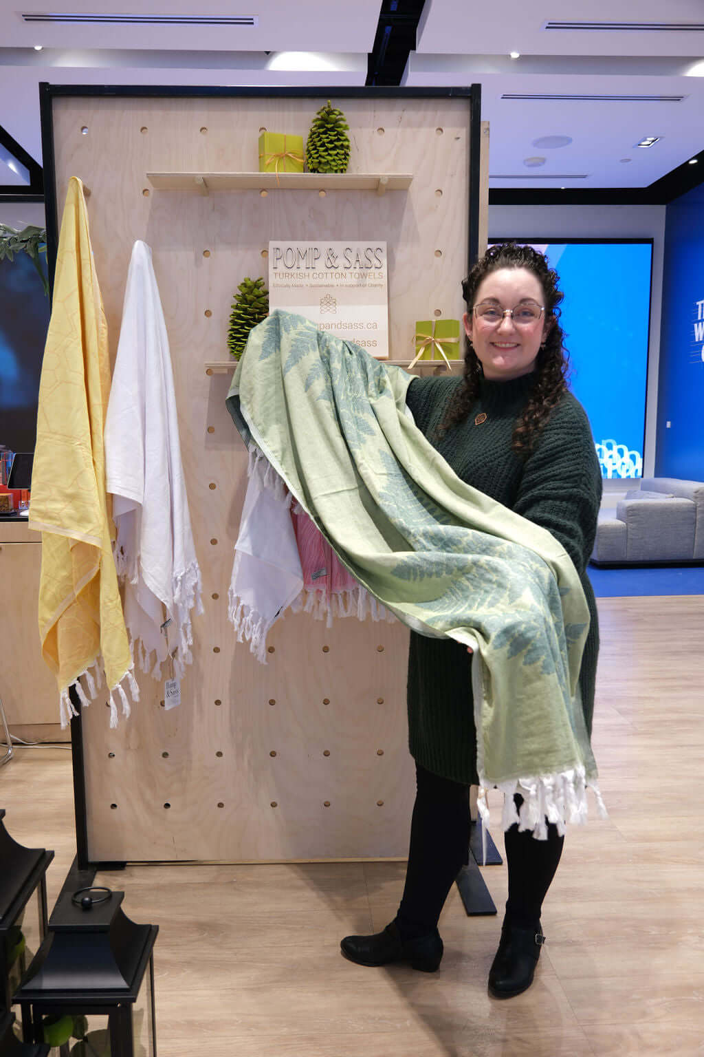 Nikky Starrett, founder of Pomp & Sass stands holding the Fern green Turkish cotton body towel at the RBC eXperience Market located in the Sherway Garden Mall 2022