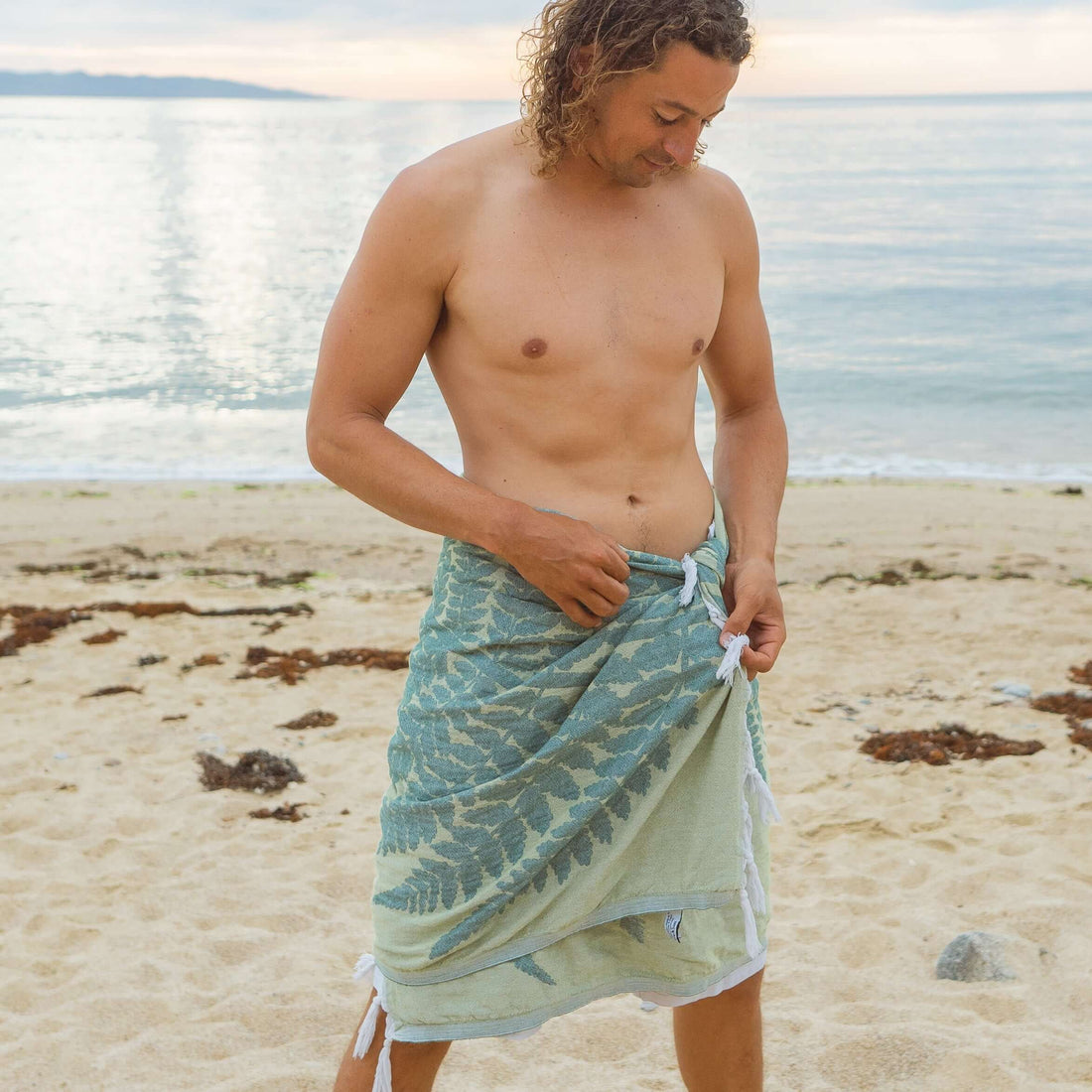 A man using a Turkish towel at the beach because he values sustainability 