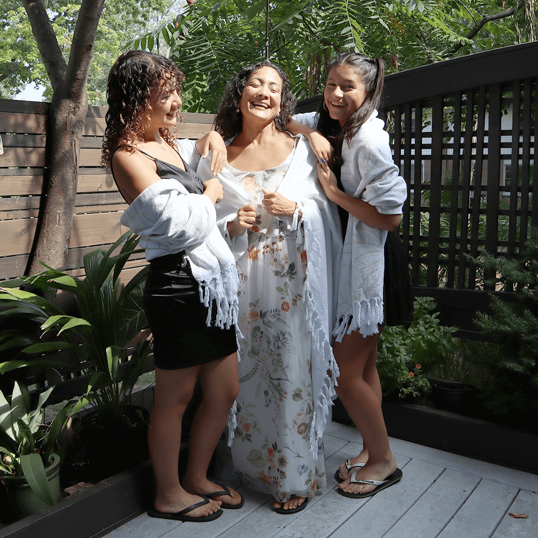 A Latina mother and two daughters laughing while draped in white Pomp & sass Turkish towels. 