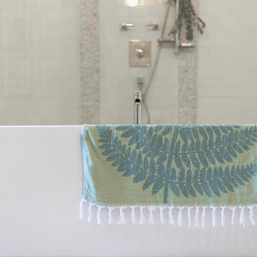 A green fern Turkish towel placed on the side of a bathtub. 