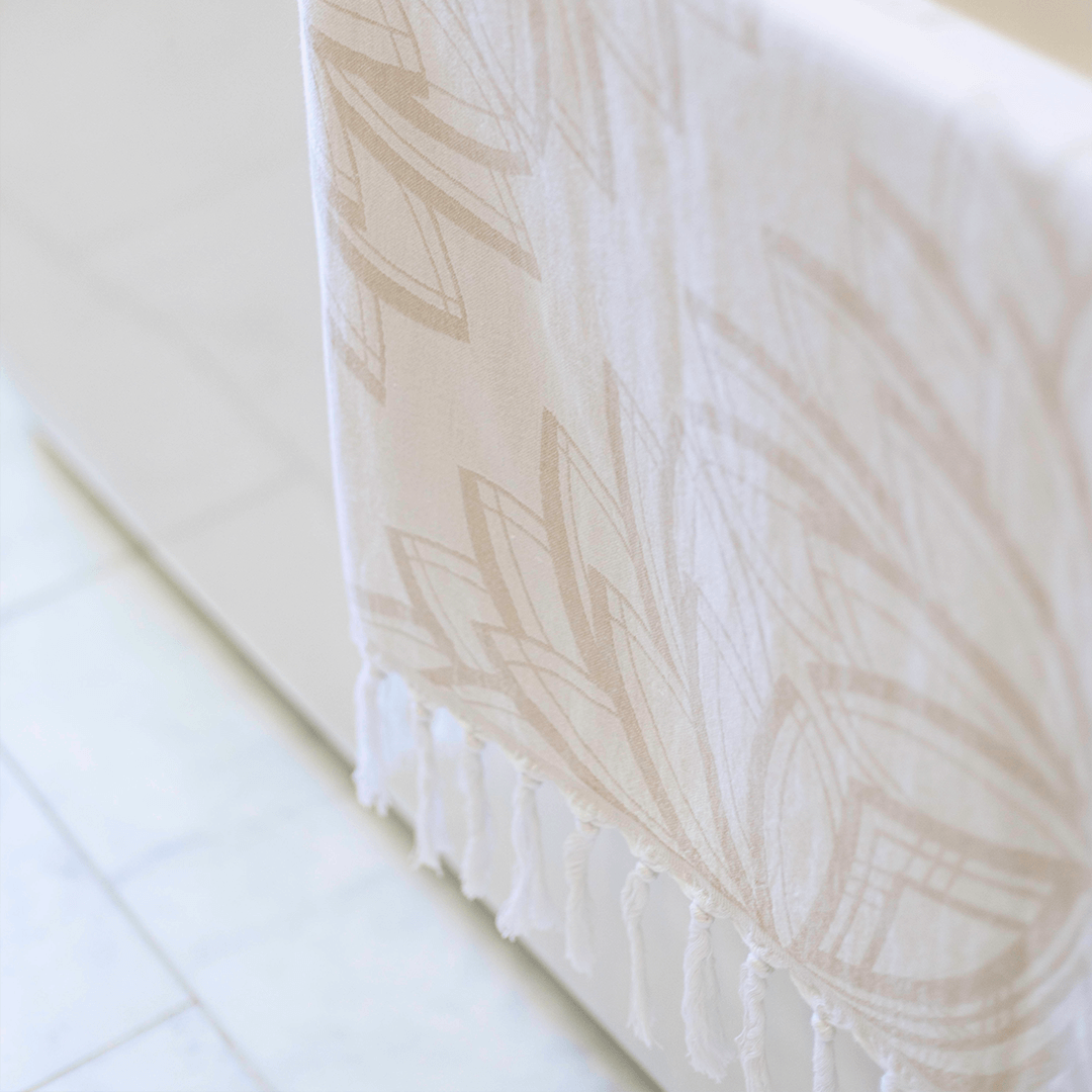 A cream coloured Lotus flower designed Pomp & Sass towel draped over the side of a bath tub. 