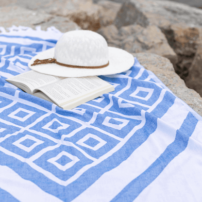Blue and white Turkish towel spread over large rocks. A book and hat wait on the towel.