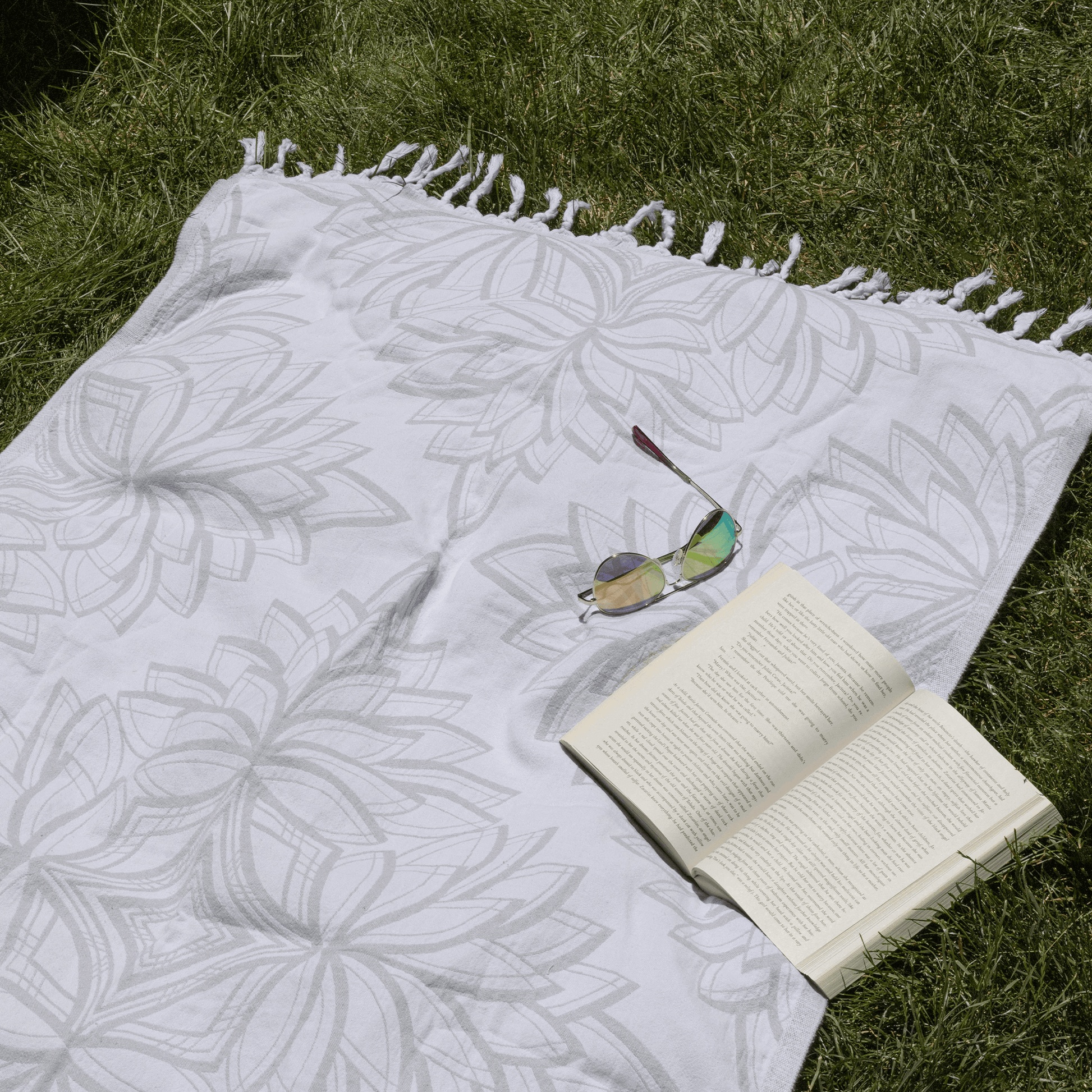 Grey and white Turkish towel on the grass with a book and sun glasses in the summer sun