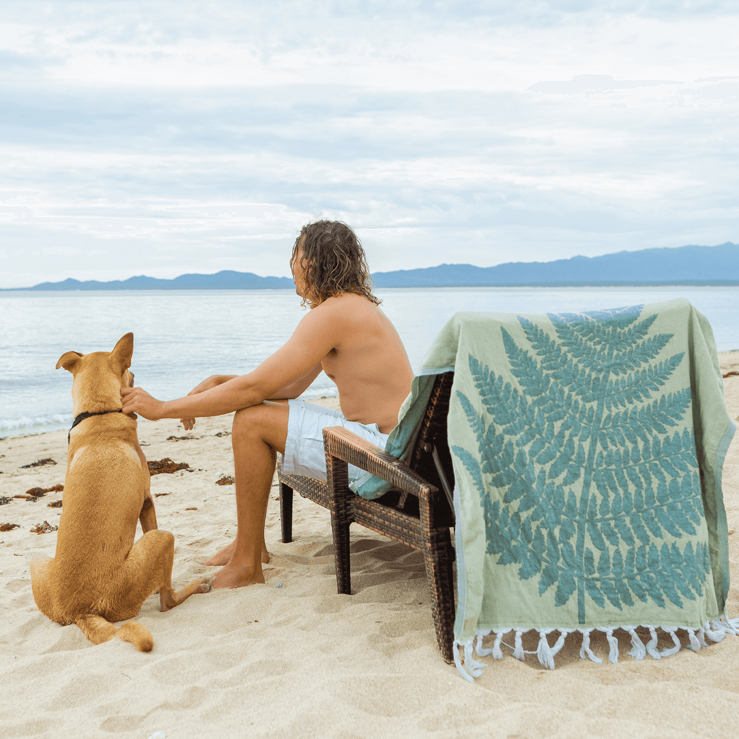 Man with dog at the beach using a green fern set of Turkish towel
