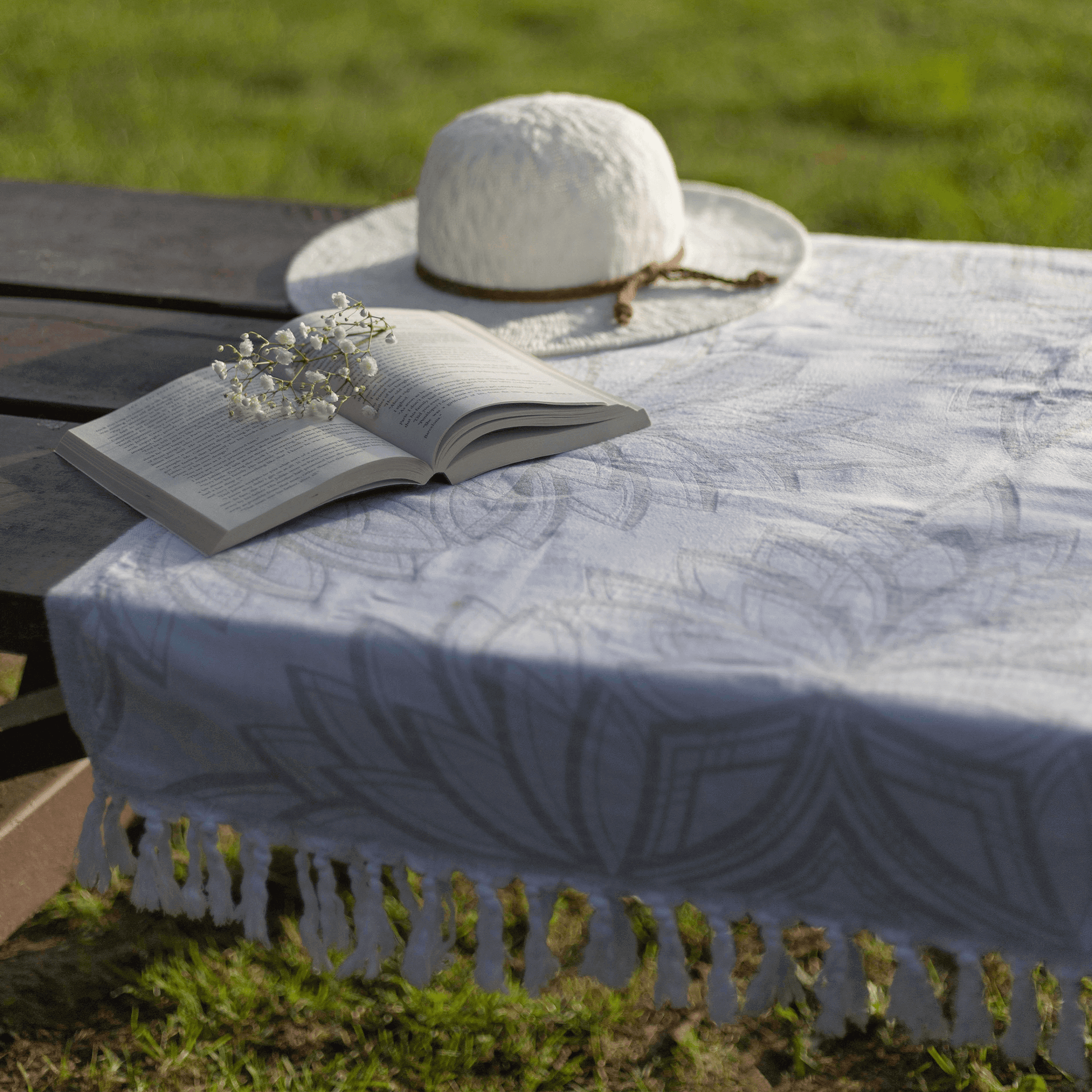 Grey and white Turkish cotton towel used as a picnic table cloth in the summer sun with a had book and sprig of babies breath flowers