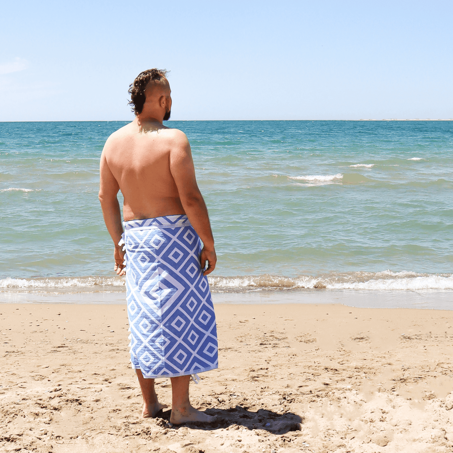Man stands on beach in summer wearing a blue and white Turkish Towel