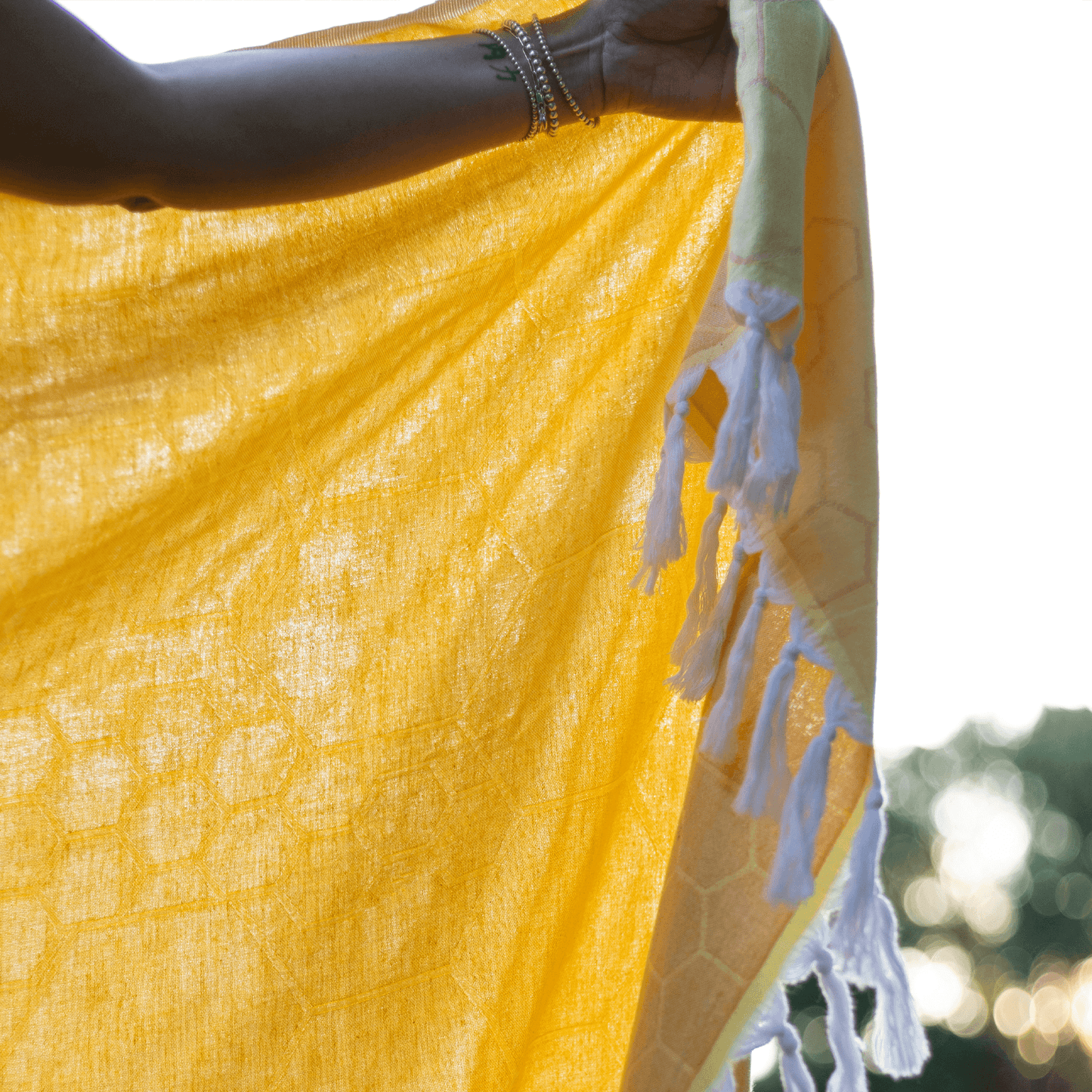Woman holds up a honeycomb yellow Turkish towel with white tassels