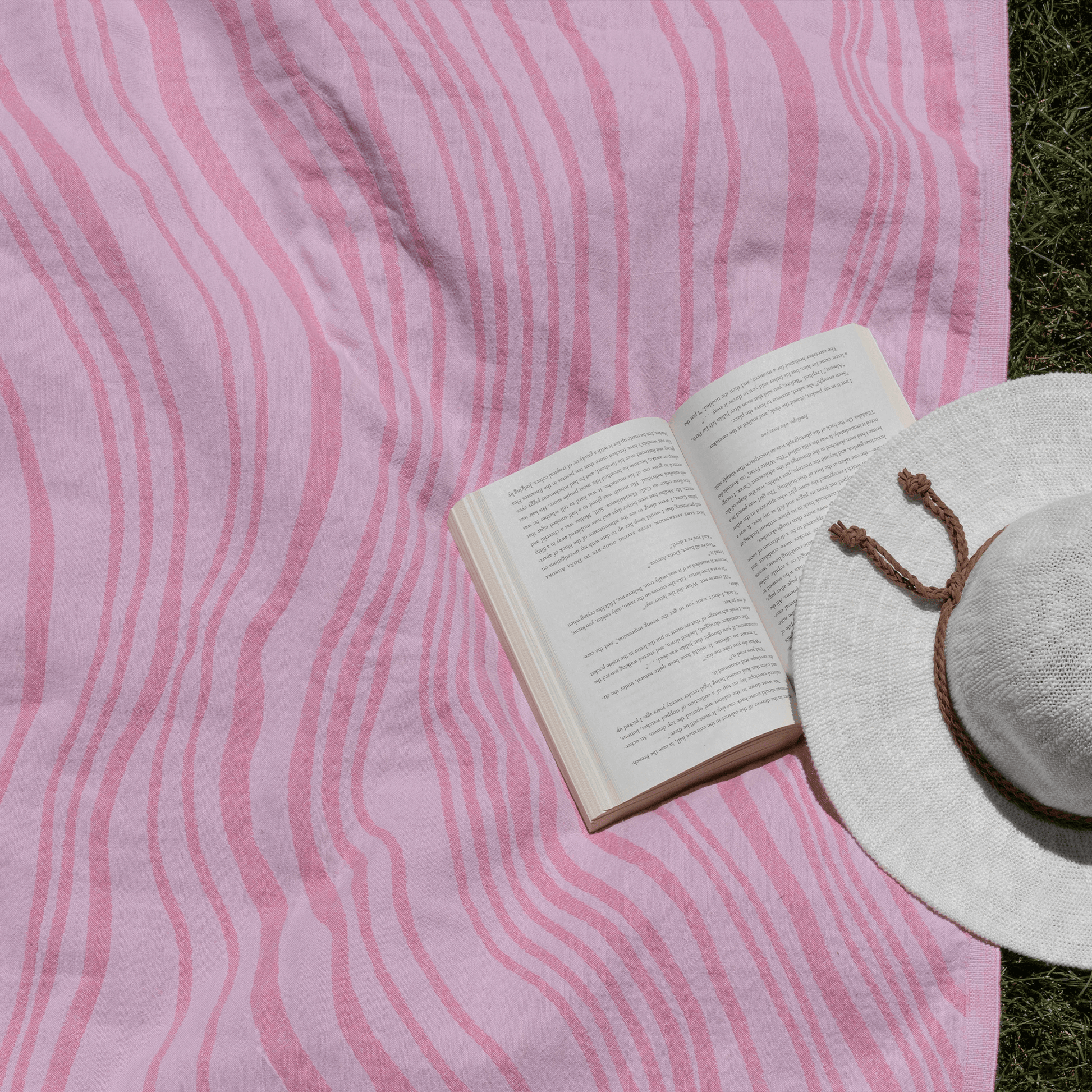 Summer grass with a pink Turkish towel, open book and hat