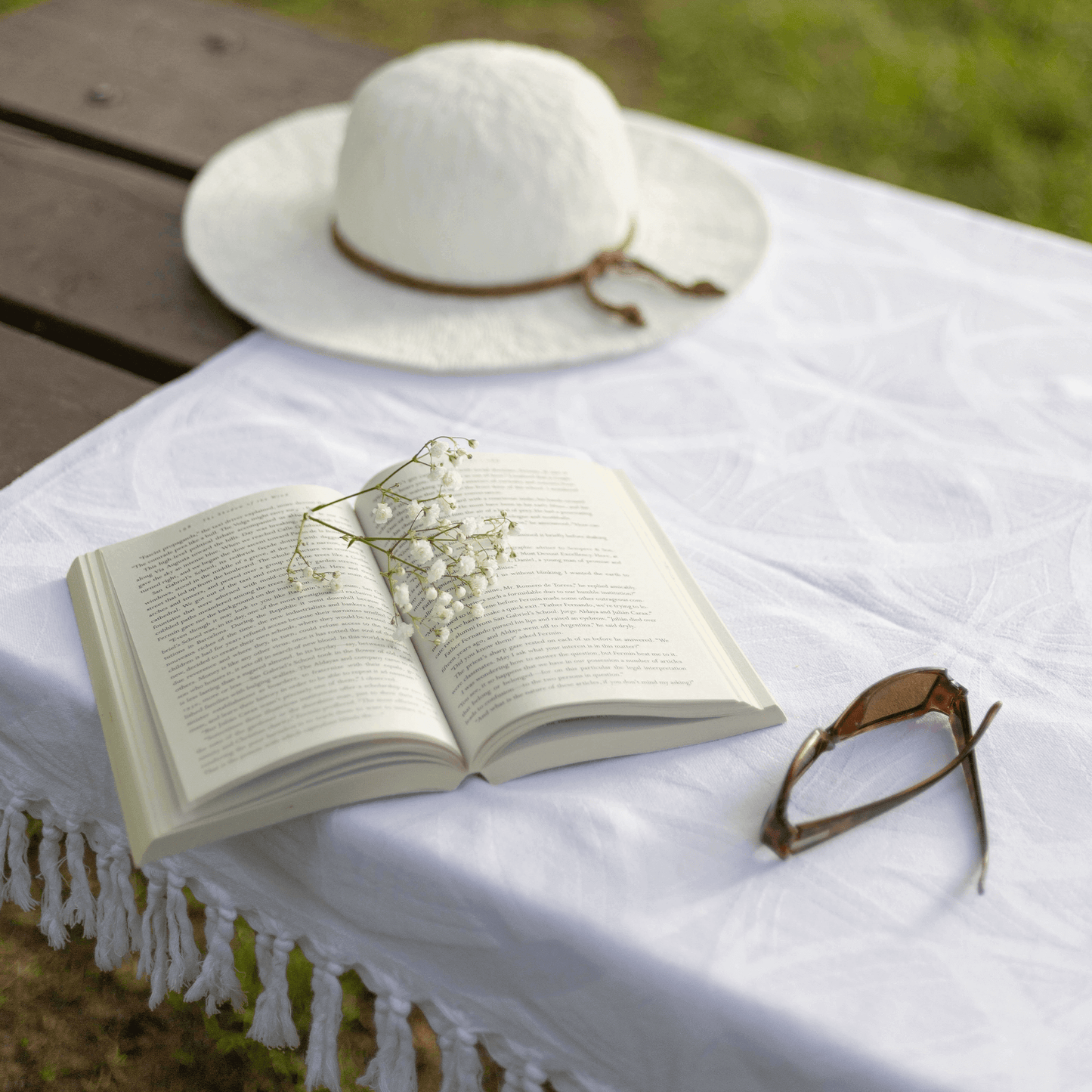 White Turkish towel used as a picnic tablecloth with a book and summer hat