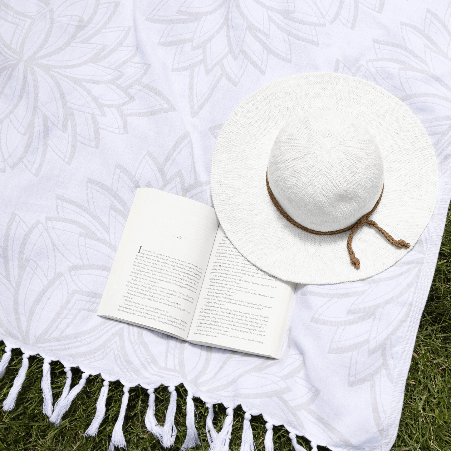 Grey and white Turkish towel with sunhat and book on the summer grass