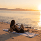 Woman using a grey and white Turkish towel on the beach at sunset