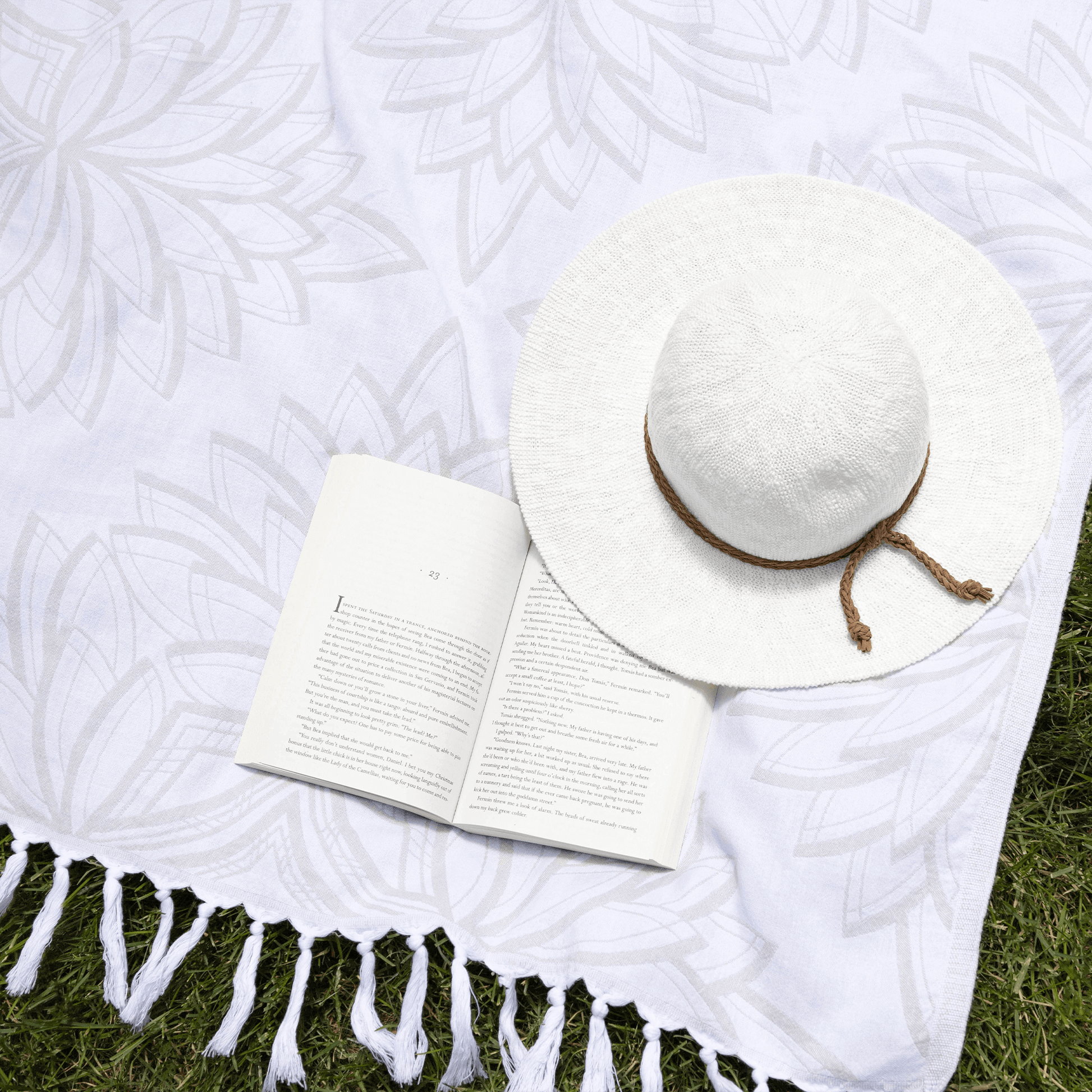 Grey and white Turkish towel on grass with a hat and book in the summer