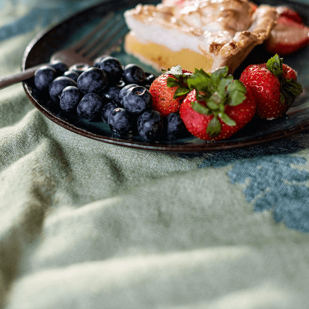 Green Turkish towel used as a tablecloth with strawberries blueberries and pie